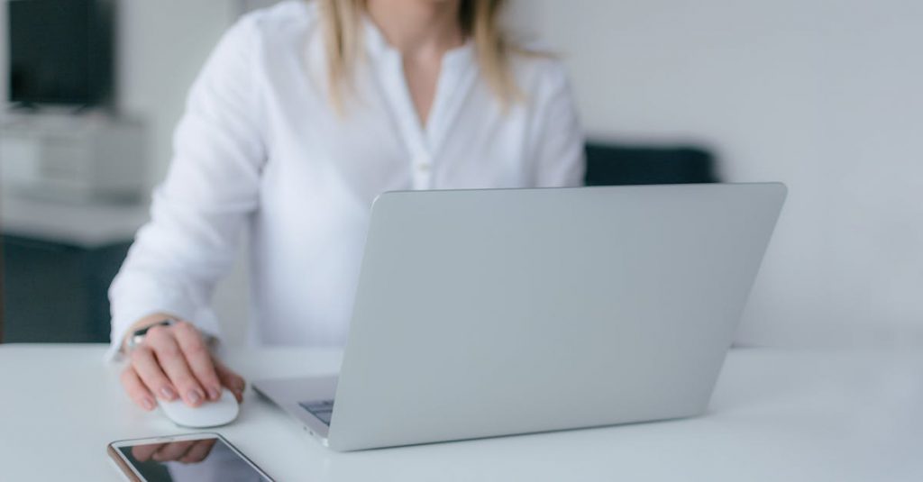 A woman working at a desk using a laptop and smartphone, exemplifying remote work.
